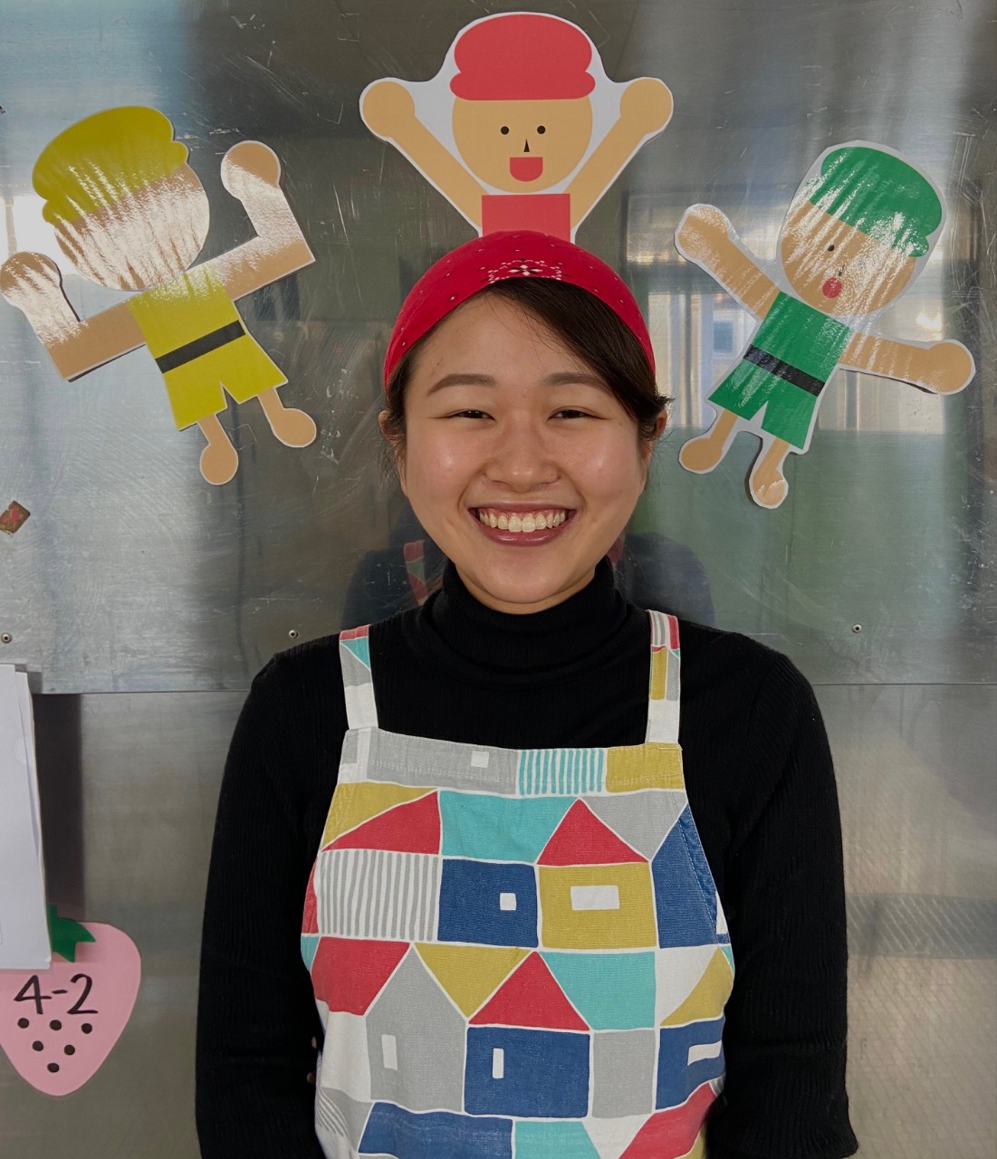 写真:窓に貼られた飾りの前に立つエプロンの女性