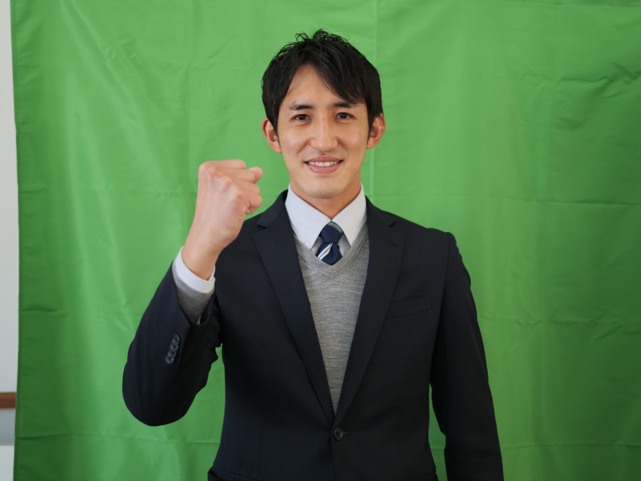 写真：グリーンバックを背にガッツポーズをするスーツの男性